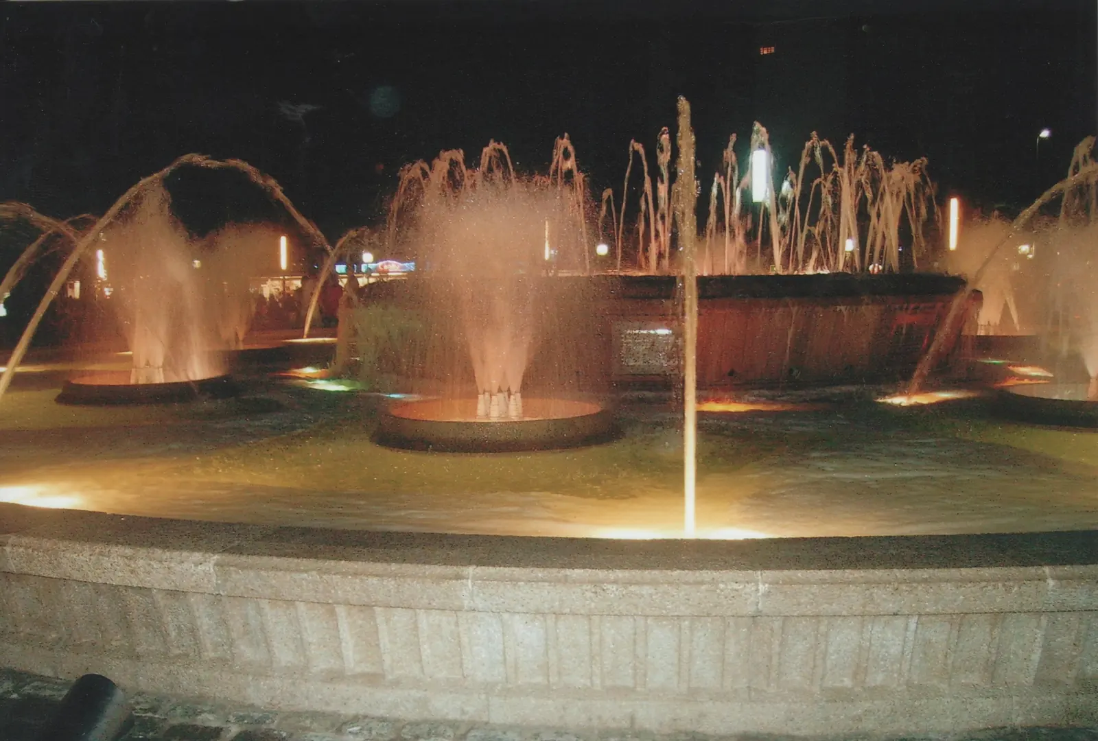 Una fuente circular en Salou con varios chorros de agua iluminados en naranja contra el cielo oscuro de la noche