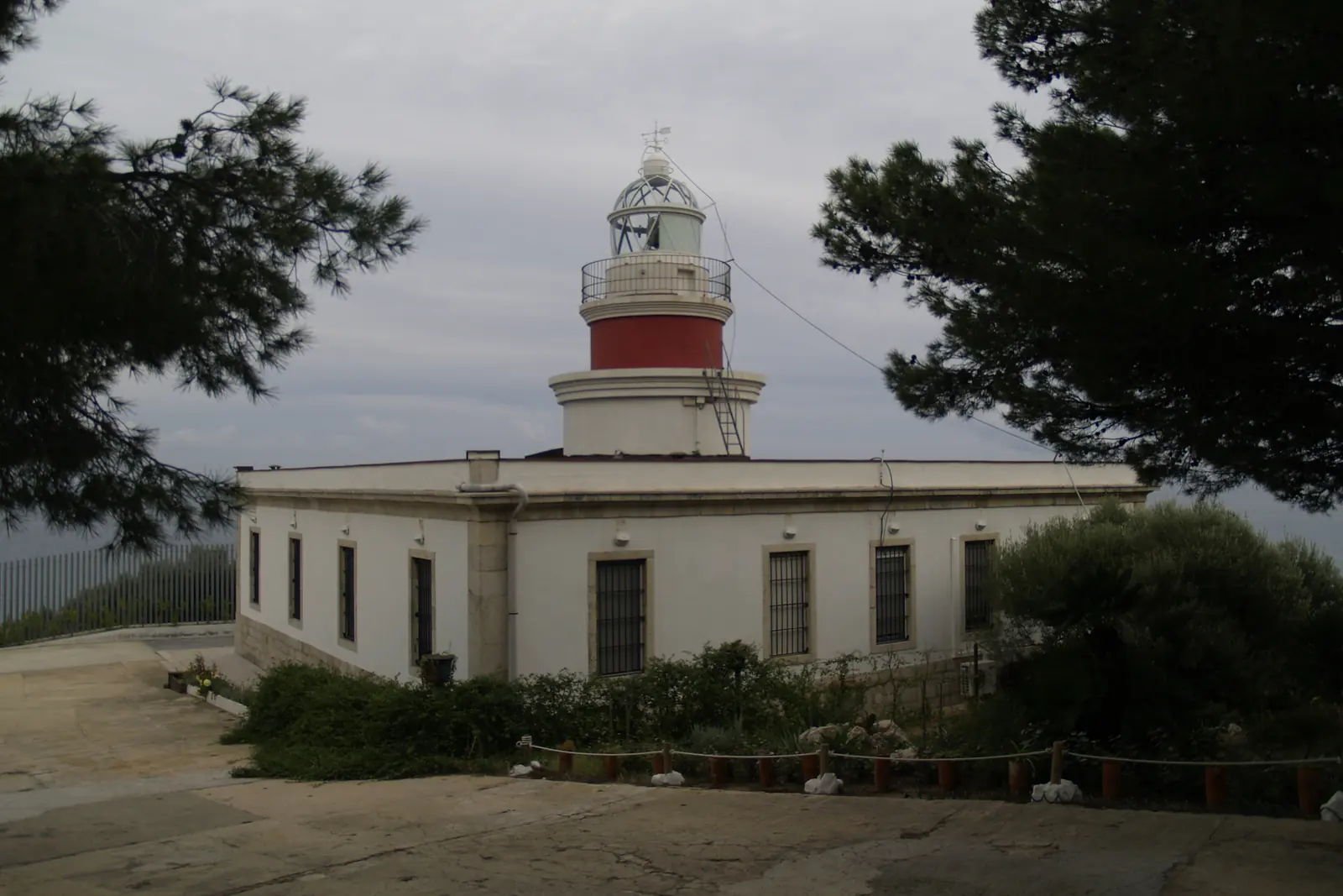 El faro de Salou, un edificio blanco con una torre roja y blanca, rodeado de pinos bajo un cielo nublado