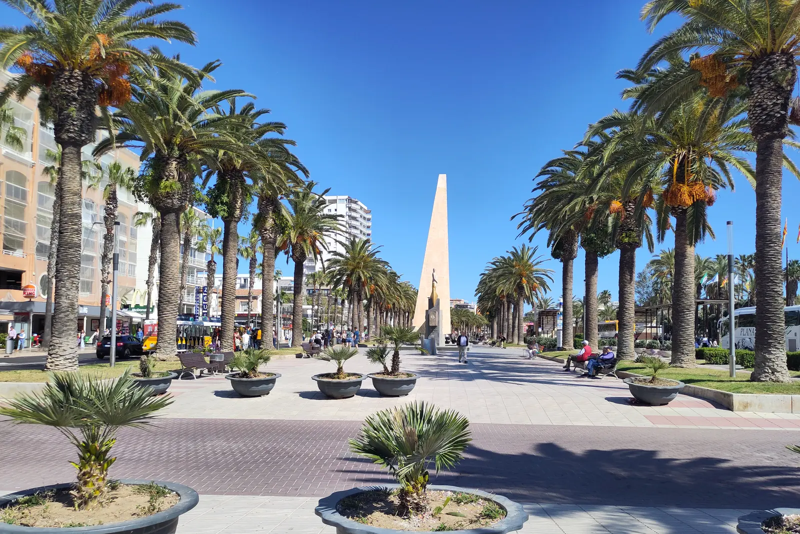 El Passeig Jaume I de Salou, una amplia promenade pavimentada flanqueada por palmeras y jardineras, que conduce hacia un esbelto obelisco